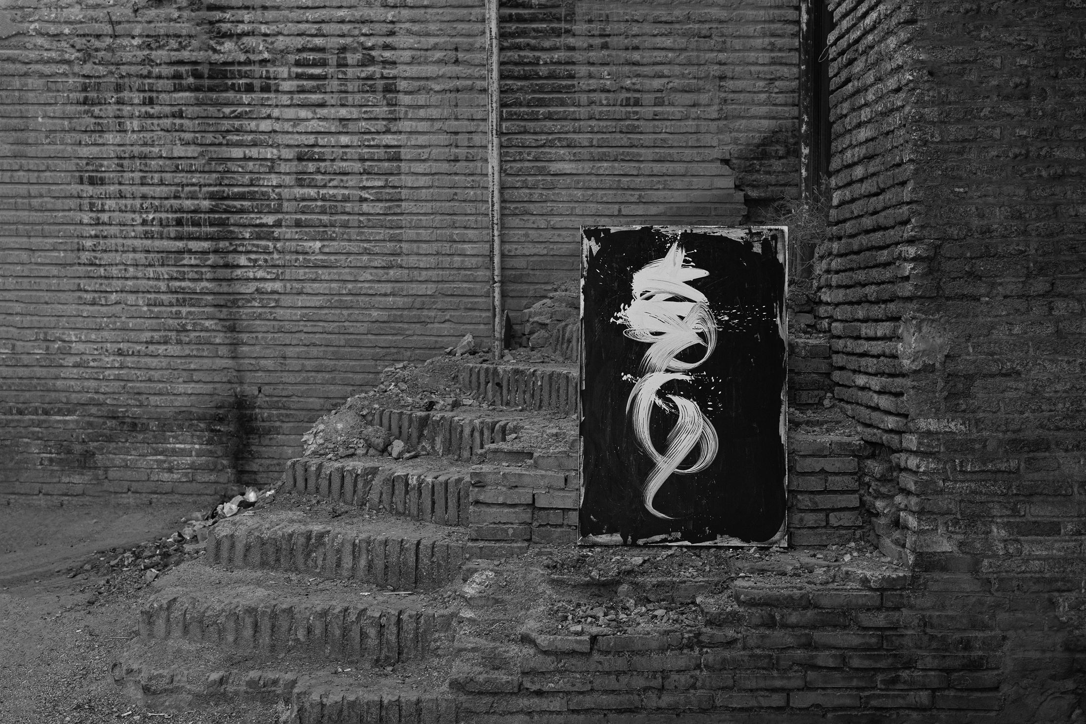 A black canvas with a single white gesture, resting on the ruined brick steps of an old house