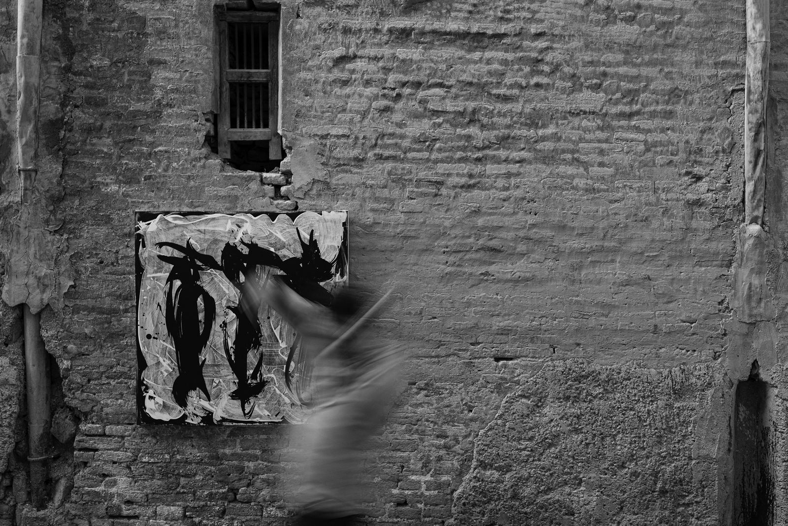 A figure blurs past a canvas hung on a brick wall