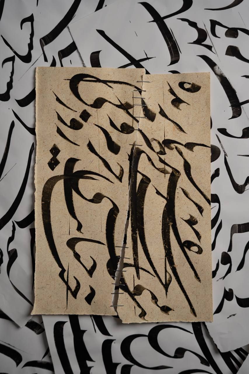 A stapled calligraphy sheet laid over a spread of printed letterforms